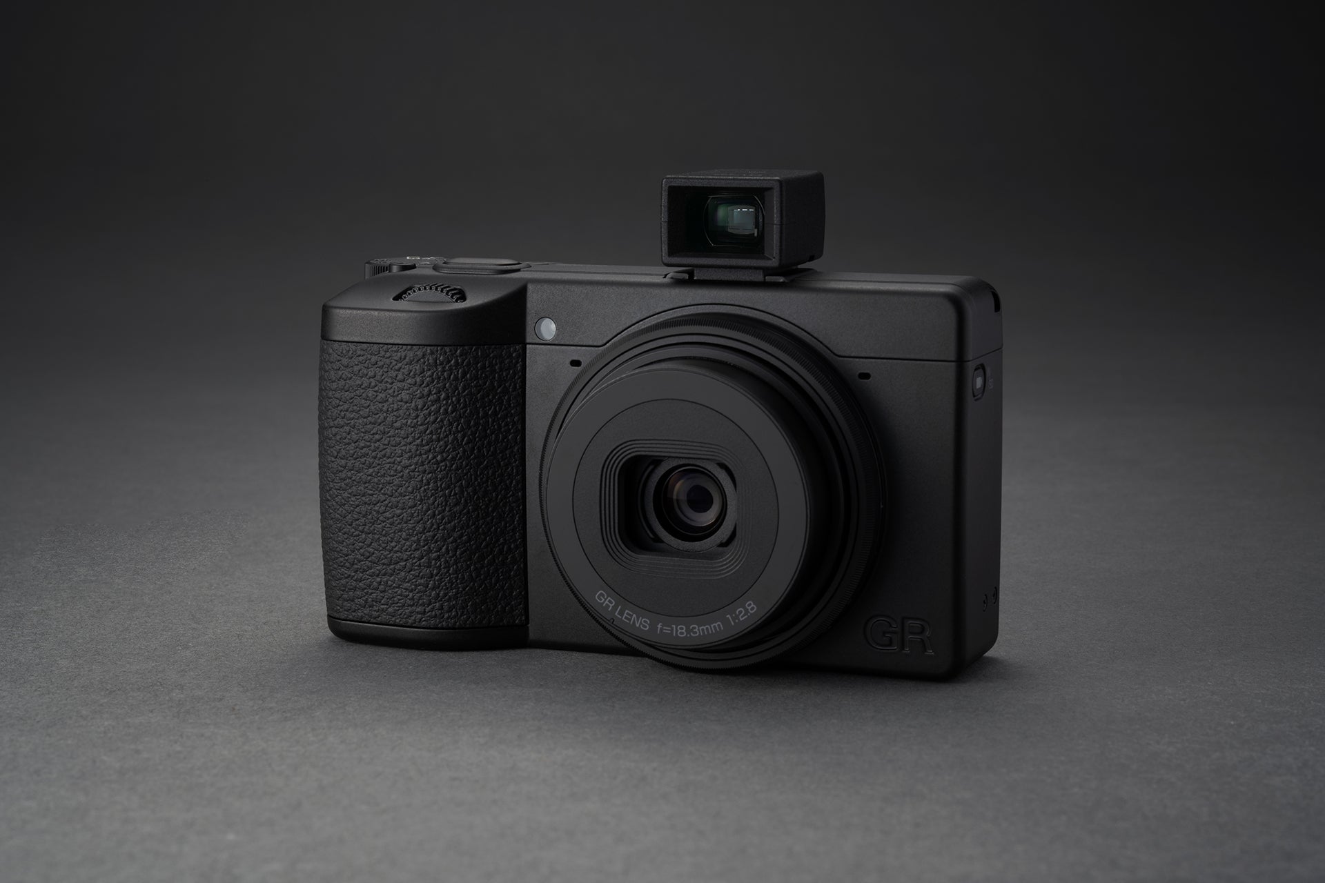 Aparat foto Ricoh GR IV Monochrom văzut din unghi lateral cu vizor optic extern montat pe patina de blitz, design compact profesional pentru fotografia de stradă.