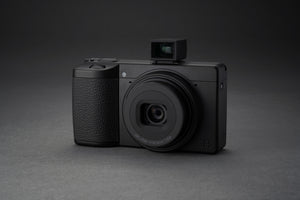 Aparat foto Ricoh GR IV Monochrom văzut din unghi lateral cu vizor optic extern montat pe patina de blitz, design compact profesional pentru fotografia de stradă.