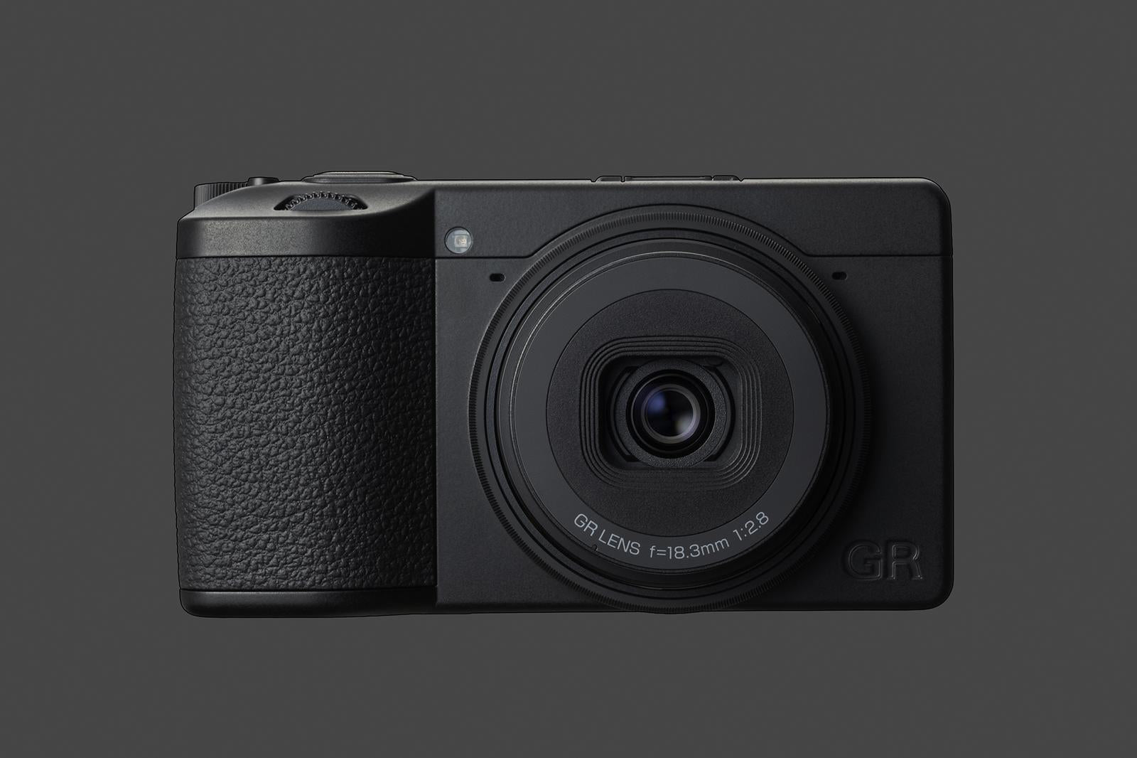 Detaliu frontal Ricoh GR IV Monochrom pe fundal gri, evidențiind grip-ul texturat, obiectivul fix f/2.8 și designul minimalist de tip "stealth".
