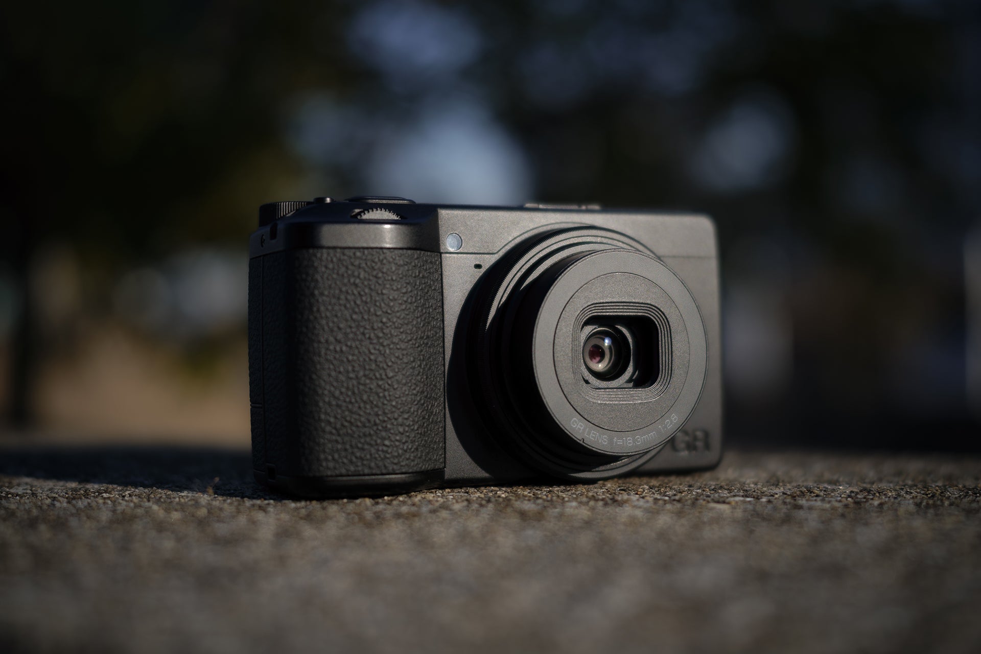 Aparat foto Ricoh GR IV Monochrom așezat pe o suprafață de piatră în exterior, evidențiind dimensiunile compacte și construcția solidă pentru fotografia de stradă.