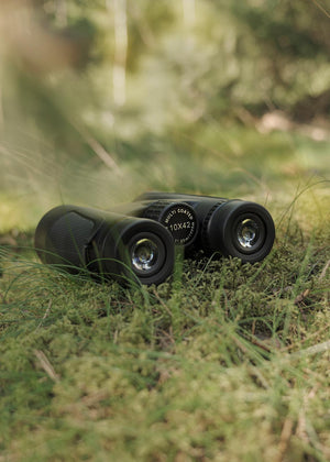 Binoclu Focus Bright 10x42 asezat pe muschi verde in padure pentru drumetii si vanatoare