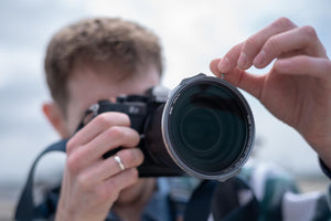Person holding a camera with a large lens against a blurred background