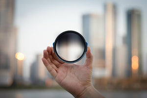 Nisi JetMag Pro Filtru Medium FS GND8 (0.9) 82mm. Hand holding a round object with blurred cityscape in the background