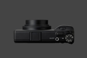Vedere superioară detaliată a camerei Ricoh GR IV Monochrom, evidențiind butonul On/Off iluminat, rotița de moduri (P, Av, Tv, M, U1-U3) și declanșatorul ergonomic.