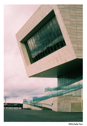 Clădire modernă cu design geometric fotografiată pe film color Harman Phoenix 200 format 120, evidențiind contrastul și granulația fină pe cer înnorat - Mostră gphoto.ro