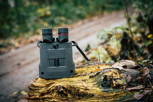 Binoclu cu stabilizare Kite APC 50 ED AA pe un buștean, cu fundal de pădure și potecă