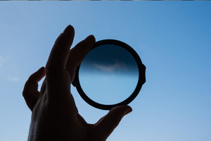 Mână de fotograf ținând filtrul magnetic circular NiSi JetMag Pro Medium FS GND8 în fața cerului albastru, evidențiind clar zona de tranziție graduală și densitatea neutră a sticlei.