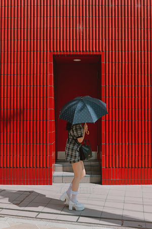 O fotografie creativă de stradă realizată cu Panasonic LUMIX S9, în care o persoană cu o umbrelă închisă la culoare trece prin fața unui perete roșu intens cu textură verticală. Imaginea demonstrează capacitatea senzorului Full Frame de a reda culori extrem de vii și detalii clare în zonele de umbră și lumină puternică.