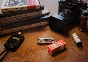 Echipament foto analog format mediu cu aparat Pentax, exponometru Sekonic și film color Harman Phoenix 200 format 120 pe o masă de lucru – gphoto.ro.