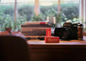 Cutii de film color Harman Phoenix 200 format 120 lângă un aparat foto Pentax 67, într-un decor creativ cu lumină naturală – gphoto.ro.