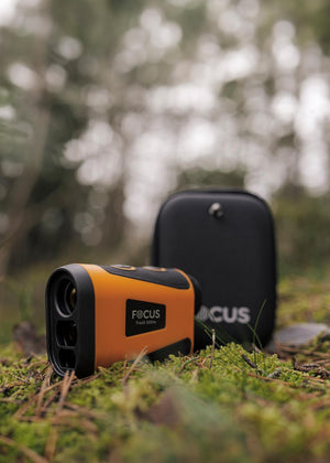 Telemetru laser Focus Track RF 500m alături de husa sa de protecție pe mușchi de pădure în natură