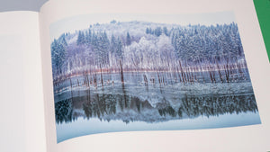 Albumul de artă „Cuejdel” deschis la pagina ce prezintă fotografia intitulată „My Lake”, selectată ca „Photo of the Day” de nationalgeographic.com. Imaginea surprinde o reflexie spectaculoasă de iarnă pe suprafața lacului Cuejdel, cu o pădure de brazi ninsă și chiciură care se oglindește perfect în apa înghețată, creând o simetrie naturală fascinantă. Această lucrare emblematică subliniază măiestria fotografului în capturarea momentelor unice din sălbăticia Carpaților.