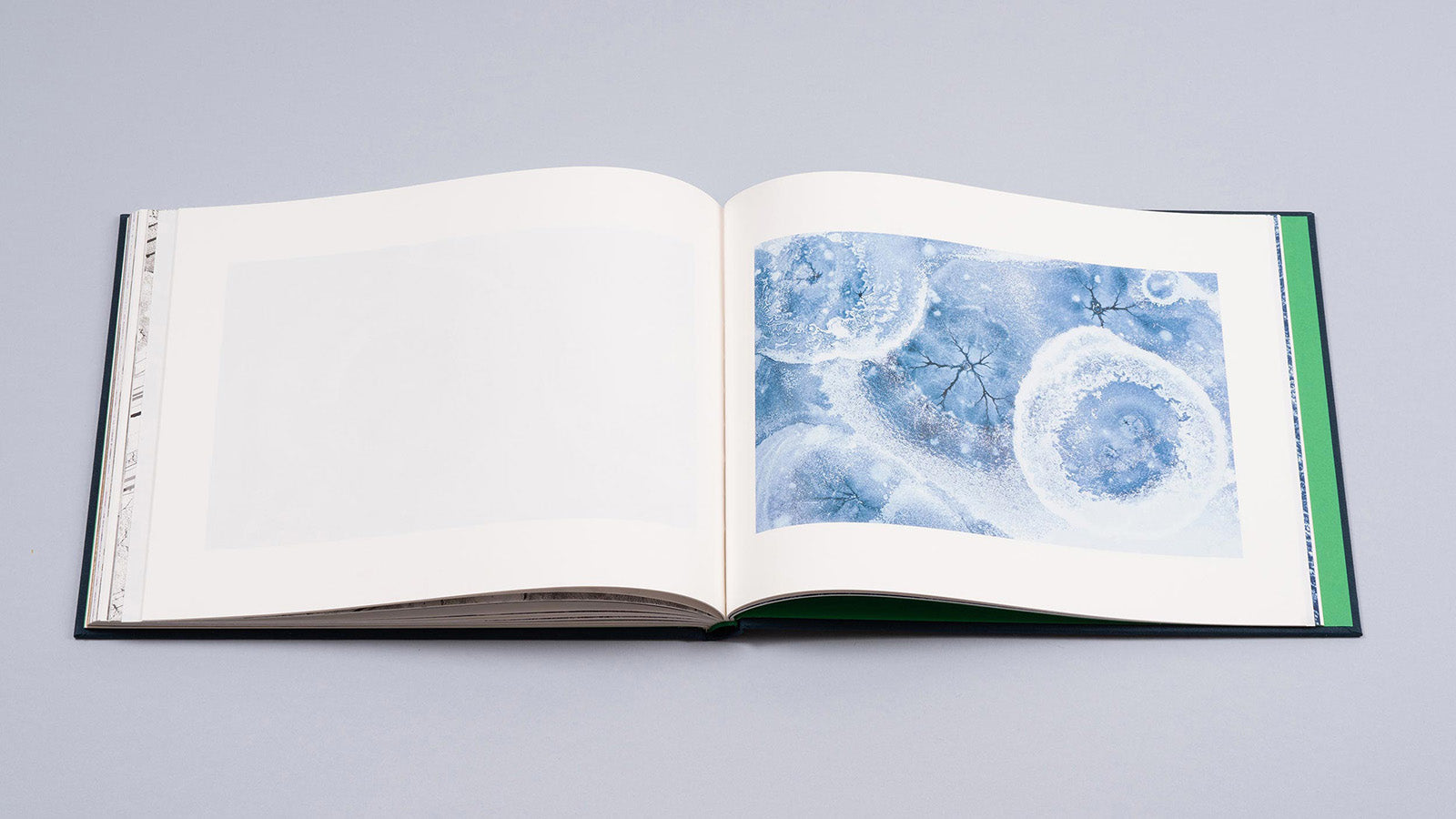 Albumul de artă fotografică „Cuejdel” de Gheorghe Popa, deschis la o pagină ce prezintă o fotografie abstractă a suprafeței înghețate a lacului Cuejdel. Imaginea surprinde modele organice și fractale de un albastru rece și alb, formate în mod natural pe gheață. Designul minimalist cu margini albe pune în valoare complexitatea și fragilitatea acestor texturi naturale din Carpați.