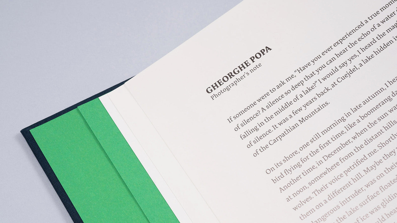 Detaliu din interiorul albumului „Cuejdel” deschis la pagina intitulată „Photographer’s note” semnată de Gheorghe Popa. Textul începe cu o reflecție despre liniștea profundă a lacului și experiența personală în sălbăticia Munților Carpați. Designul paginii păstrează inserția de hârtie verde smarald, oferind o estetică elegantă și unitară întregului volum.