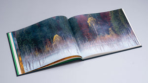 Albumul de artă fotografică „Cuejdel” deschis la o pagină dublă ce înfățișează un peisaj de toamnă la marginea lacului Cuejdel. Fotografia redă o pădure de conifere și foioase în culori de verde închis și arămiu, cu o perdea de ceață albă care plutește deasupra apei, evidențiind siluetele copacilor scufundați.